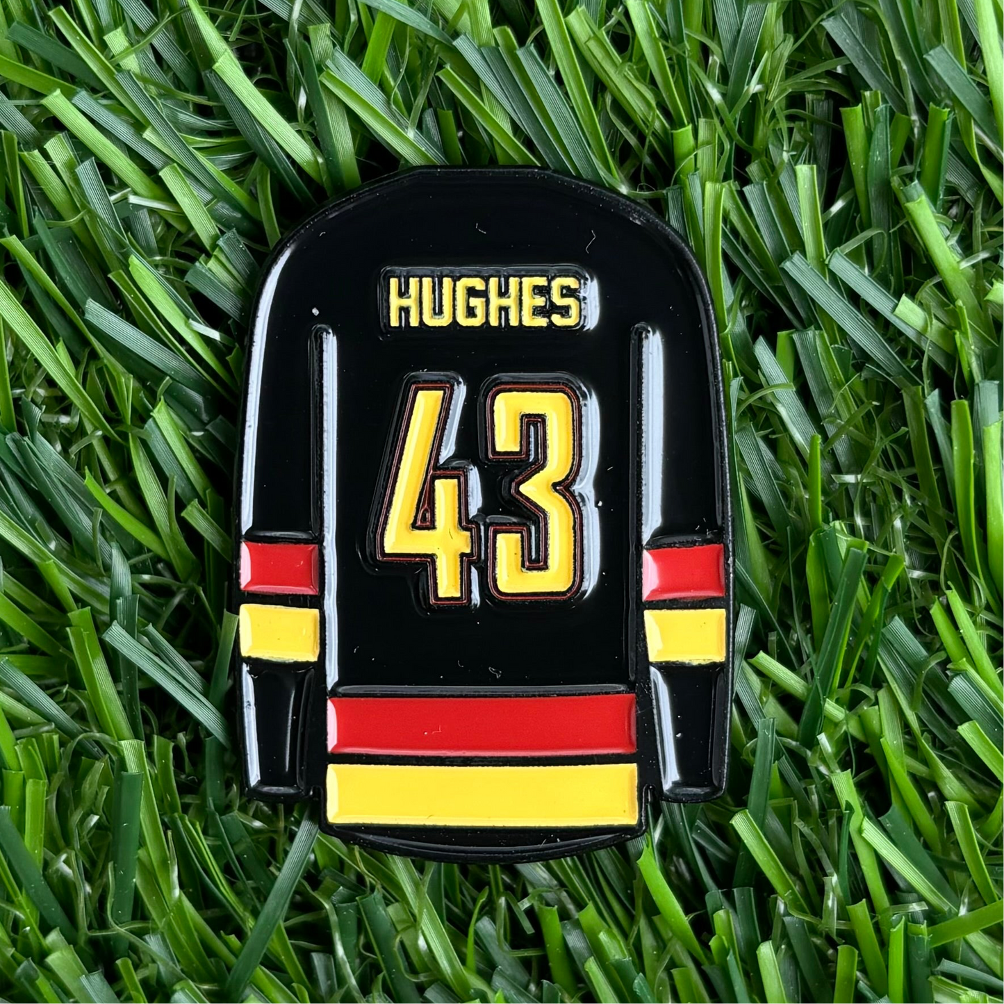 Quinn Hughes golf ball marker featuring jersey design on green grass, custom and durable golfing accessory.