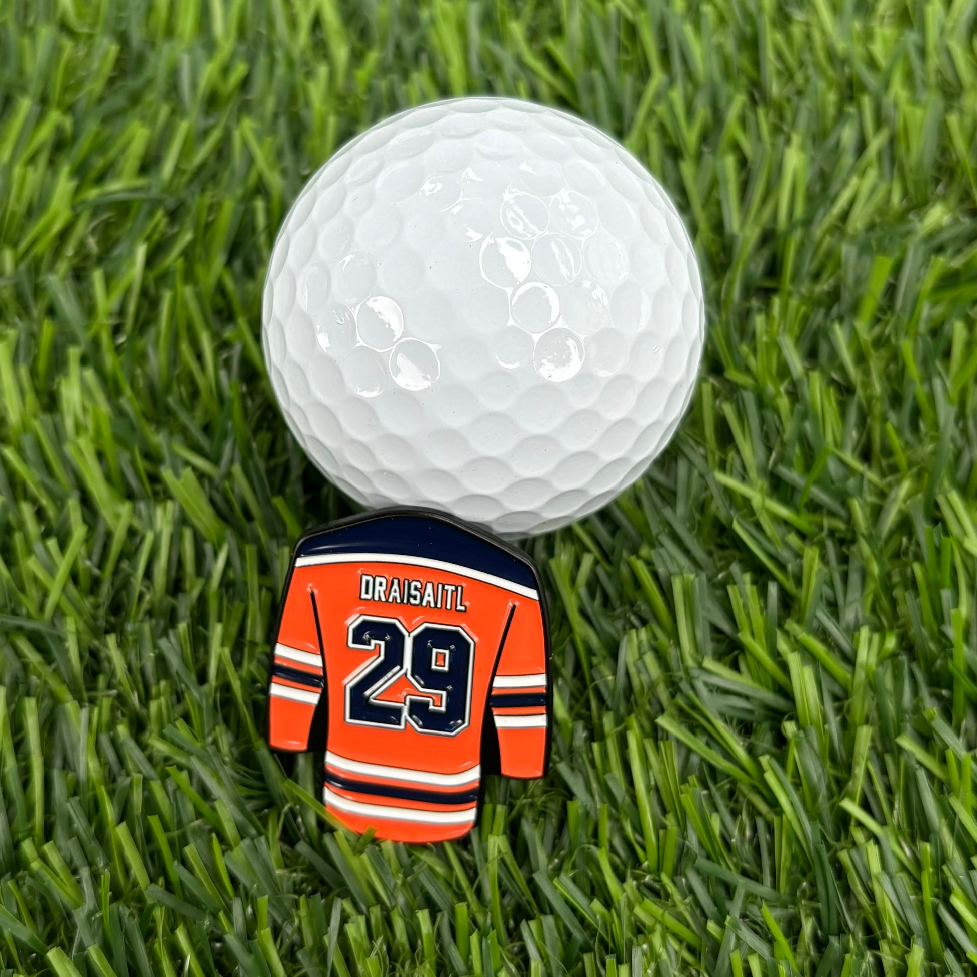 Leon Draisaitl custom golf ball marker shaped like a sports jersey next to a golf ball on green grass