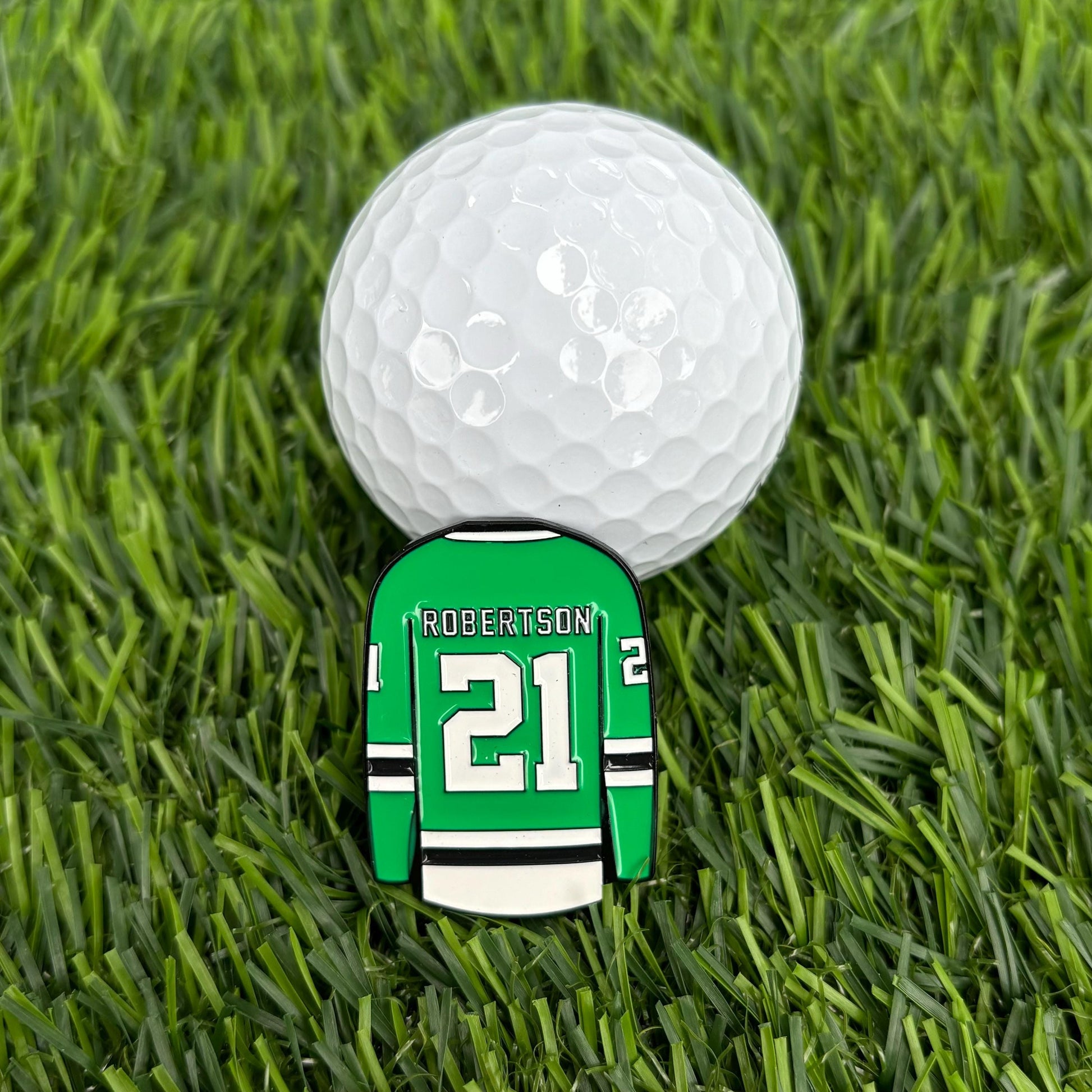 Jason Robertson golf ball marker shaped like a green hockey jersey with number 21 next to a golf ball on grass.