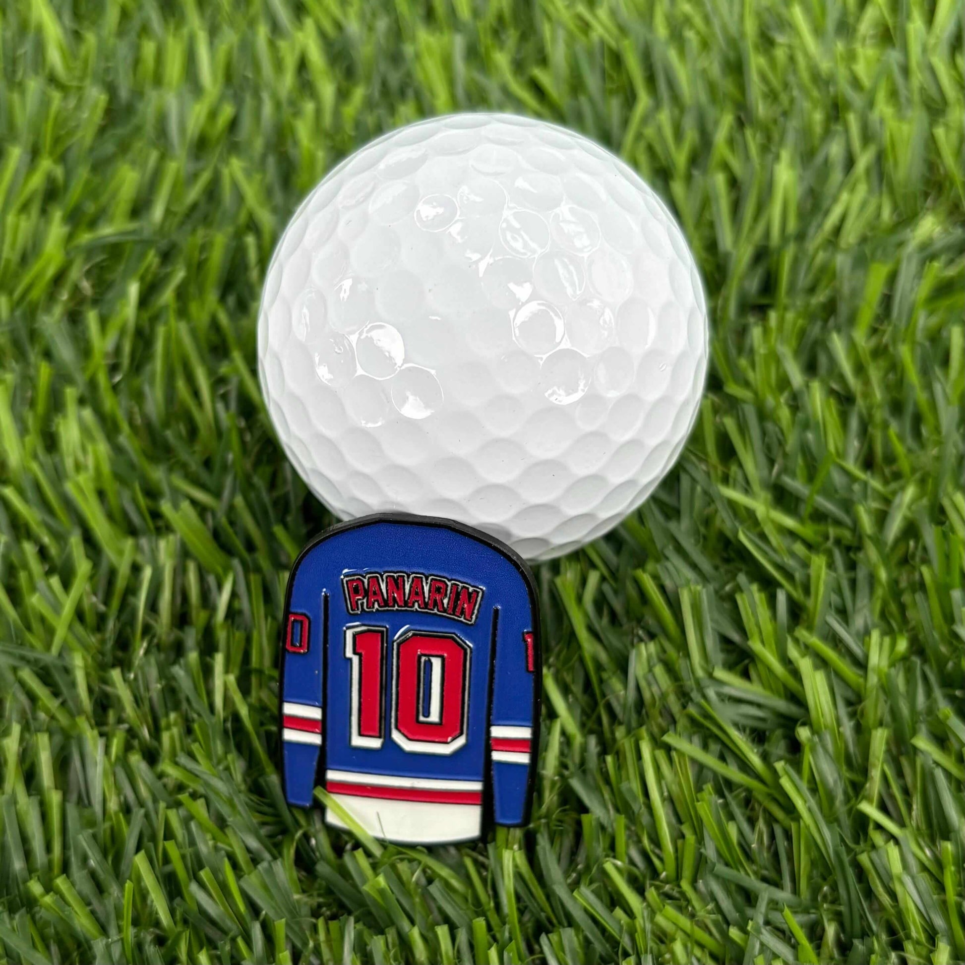 Artemi Panarin golf ball marker on grass next to golf ball. Stylish collectible durable premium golf accessory for enthusiasts.